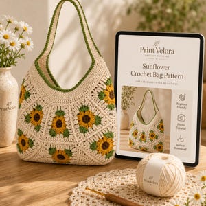 May include: A cream-colored crochet bag featuring a sunflower motif with yellow petals and dark brown centers, accented by green leaves. Beside it is a tablet displaying the text Print Velora Sunflower Crochet Bag Pattern, a ball of yarn, and a hook.