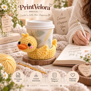 Puede incluir: Una funda de ganchillo amarilla con forma de pato, con cabeza redonda, pico naranja y mejillas rosas, que envuelve un vaso de papel blanco con estampado de hojas verdes. La funda está sobre un posavasos de madera, rodeada de lana y un ganchillo.