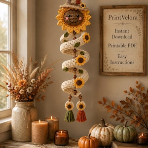May include: A crocheted spiral wall hanging featuring a smiling sunflower face at the top, wearing a brown hat. The cream-colored spiral body is decorated with small sunflowers and green leaves, ending in two sunflower-topped tassels in green and orange.