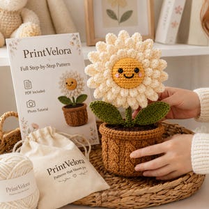 May include: A crocheted sunflower with a yellow face, white petals, and green leaves in a brown cable-knit pot. Beside it is a PrintVelora instruction card and a small beige drawstring bag with the PrintVelora logo and text Patterns that bloom joy.