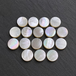 May include: A collection of seventeen circular mother of pearl buttons arranged in a cluster. Each button features a smooth, polished surface with a natural iridescent sheen, displaying subtle variations of white, cream, and soft rainbow reflections.