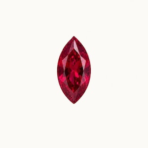 May include: A marquise-cut gemstone with a deep, vibrant red color. The stone features a symmetrical, elongated shape with pointed ends and multiple triangular facets that create a reflective, brilliant surface across the entire face of the gem.