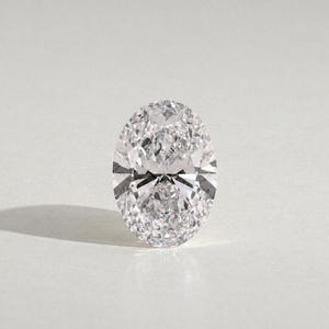 Può includere: Una gemma trasparente e incolore con taglio ovale, caratterizzata da numerose sfaccettature triangolari e a forma di aquilone che creano una superficie brillante e riflettente. La pietra mostra un'elevata dispersione della luce.