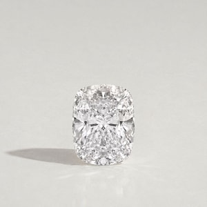 Op de afbeelding: Een kussengeslepen diamant met een briljant, symmetrisch facetpatroon. De kleurloze edelsteen wordt gepresenteerd tegen een neutrale achtergrond, die de helderheid en glans benadrukt. De vorm van de diamant is rechthoekig met afgeronde hoeken.