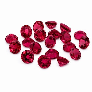 May include: A collection of round, faceted loose gemstones in a vibrant, deep red color. Each stone features a brilliant cut with multiple triangular facets that reflect light, creating a sparkling appearance across the group of small, circular gems.