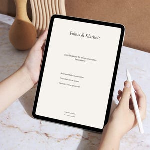 Könnte beinhalten: Ein Tablet mit dem deutschen Text "Fokus & Klarheit" und weiteren Texten, darunter "Dein Begleiter für einen bewussten Feierabend". Eine Hand hält einen weißen Stift. Der Bildschirm zeigt hellen Text auf hellem Hintergrund.