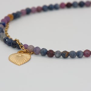 Peut inclure: Un collier de perles avec un pendentif en forme de cœur doré. Le collier est composé de petites perles à facettes dans les tons de bleu, de violet et de rose. Le pendentif en forme de cœur doré a un motif texturé en forme de soleil.