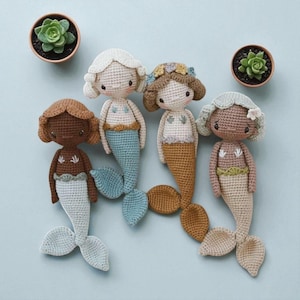 Puede incluir: Cuatro muñecas de sirena hechas a mano con ganchillo, con varios tonos de piel, colores de pelo y colores de cola. Cada muñeca tiene una cara detallada y lleva un top de ganchillo. Dos pequeñas suculentas en macetas están colocadas.