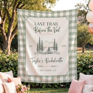May include: A rectangular fabric backdrop featuring a sage green and white buffalo check border. The center displays the text "LAST TRAIL Before the Veil", "EST. 2026", "Taylor's Bachelorette", and "LAKE TAHOE, CA" with a mountain and tent illustration.