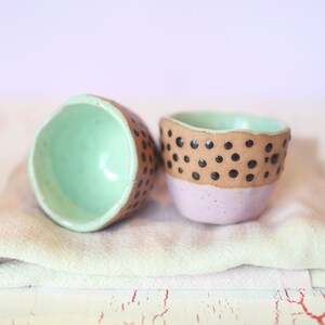 May include: Two small ceramic bowls with a speckled brown and black design. One bowl is light green on the inside and the other is light purple on the inside.