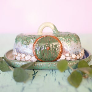 Pu&ograve; includere: Un burriera in ceramica a forma di buco di hobbit, verde e marrone. Il coperchio ha una maniglia e una porta rotonda verde. La base &egrave; verde con interno blu. Il piatto misura circa 15 cm di diametro.