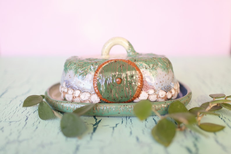 Pu&ograve; includere: Un burriera in ceramica a forma di buco di hobbit, verde e marrone. Il coperchio ha una maniglia e una porta rotonda verde. La base &egrave; verde con interno blu. Il piatto misura circa 15 cm di diametro.