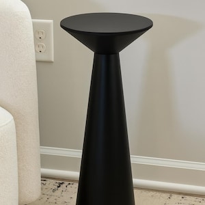 May include: A black side table with a conical base and a round top. The table has a matte finish. The table is approximately 71 cm tall. It is a modern piece of furniture.