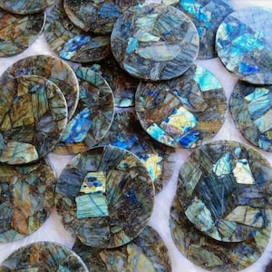 May include: A collection of round, polished labradorite coasters. Each coaster features a mosaic of blue, green, and brown tones, creating a unique, natural pattern. The coasters are approximately 4 inches in diameter.