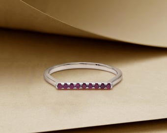 May include: A silver ring featuring a row of small, vibrant red gemstones. The ring has a simple, elegant design with a thin band and a linear arrangement of the gemstones, creating a minimalist aesthetic. The gemstones are set close together.