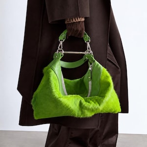 May include: A bright lime green handbag featuring a textured faux fur body and smooth leather trim. The bag includes a silver-toned metal top handle, a matching leather shoulder strap, and a central silver zipper closure with a metallic pull tab.