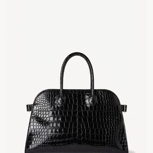Puede incluir: Bolso de mano negro brillante con textura de piel de cocodrilo. El bolso tiene una parte superior redondeada, un asa curva y dos peque&ntilde;as hebillas en los laterales. Fondo blanco.