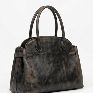 May include: A dark gray leather handbag with two top handles and a structured silhouette. The bag features a rounded top, a rectangular base, and a buckle detail on the sides. The leather has a distressed, vintage appearance.