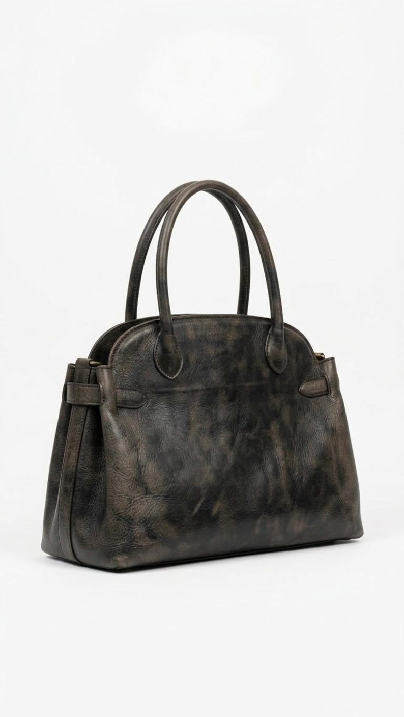 May include: A dark gray leather handbag with two top handles and a structured silhouette. The bag features a rounded top, a rectangular base, and a buckle detail on the sides. The leather has a distressed, vintage appearance.
