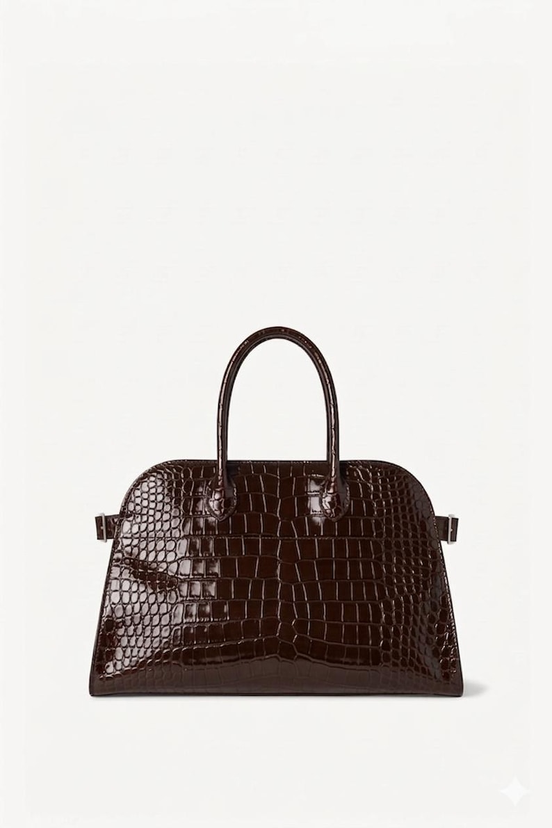 Puede incluir: Un bolso estructurado marr&oacute;n oscuro con una textura brillante de piel de cocodrilo. El bolso tiene una parte superior curvada, un asa corta y una base rectangular. Cuenta con herrajes m&iacute;nimos, con peque&ntilde;os cierres laterales.