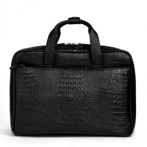 May include: Black briefcase with a textured, crocodile-like pattern. The bag features a top handle, a front zipper pocket, and a main compartment with a zipper closure. The bag is rectangular and appears to be made of leather.