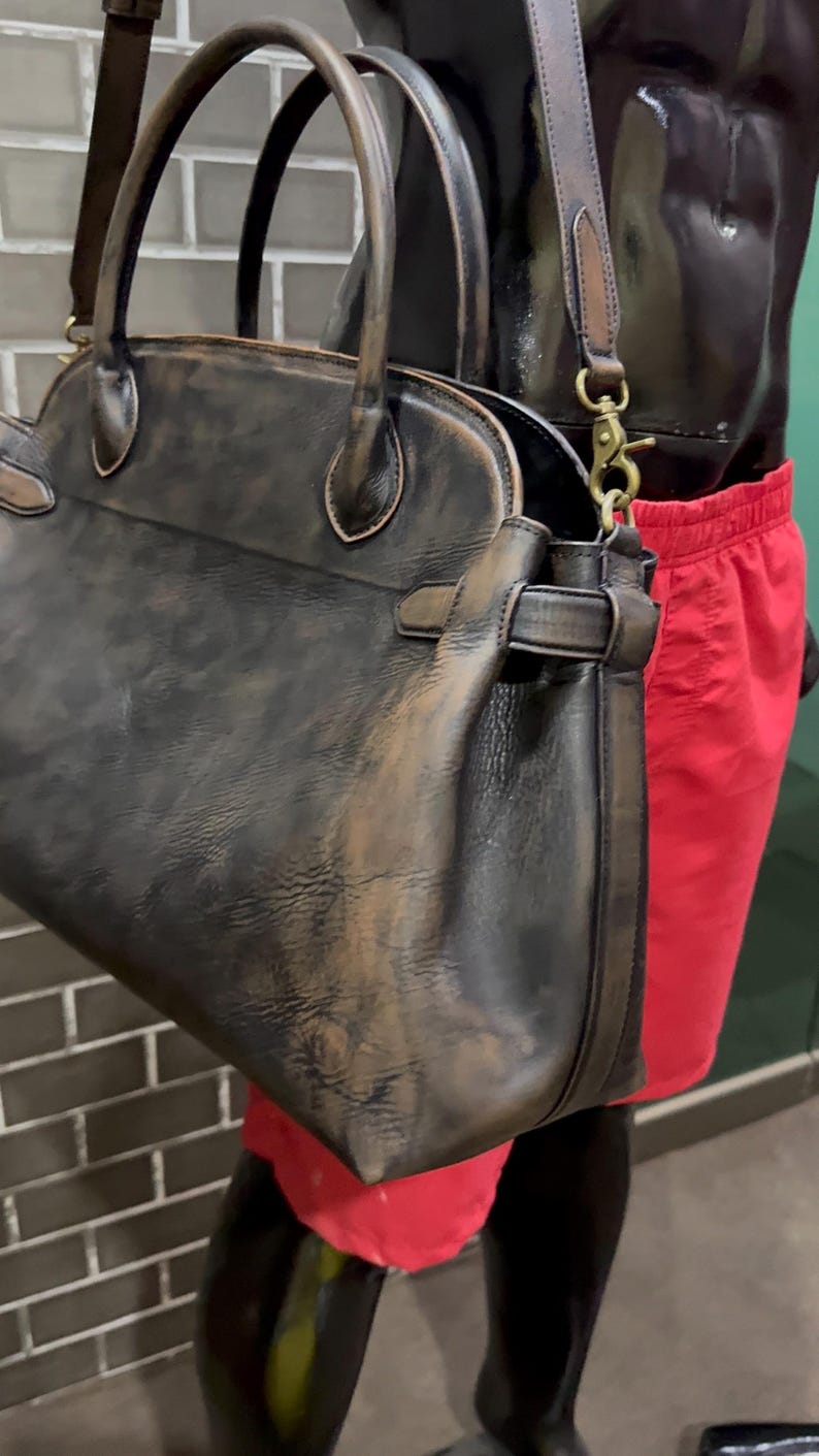 May include: A distressed leather handbag with a top handle and a detachable shoulder strap. The bag is dark brown with lighter brown accents and gold-colored hardware. The bag has a classic, structured design.
