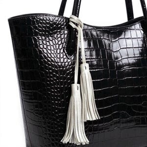 May include: Black tote bag with a crocodile skin texture. The bag has two handles and is adorned with two white leather tassels hanging from the handle. The bag is made of a shiny, patent leather material.