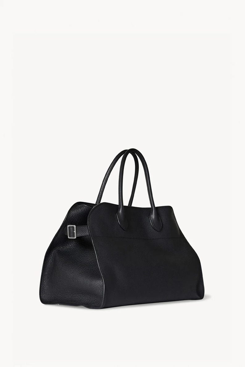 May include: A black leather tote bag with two top handles and a rectangular shape. The bag features a buckle closure on the side and a textured surface. The bag is designed for carrying items.