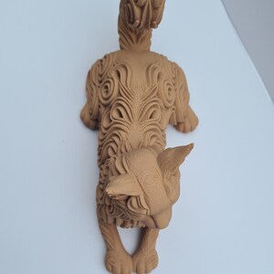 Op de afbeelding: Gedetailleerde, bruine sculptuur van een gestileerd dier, mogelijk een kat of hond, met ingewikkelde gesneden patronen. De sculptuur heeft een prominente staart en een gedetailleerd gezicht, dat een uniek artistiek ontwerp laat zien.