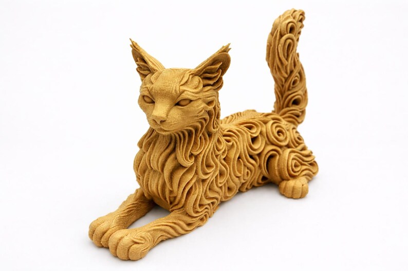 Op de afbeelding: Een gedetailleerde, goudkleurige kattenbeeldhouwwerk in een ontspannen pose. De vacht van de kat is ingewikkeld ontworpen met wervelende patronen. De sculptuur heeft spitse oren en een lange, gekrulde staart, rustend op een witte ondergrond.