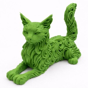Op de afbeelding: Een groene kattenbeeldhouwwerk in een liggende houding. De vacht van de kat is gedetailleerd met een wervelend patroon. Het beeldhouwwerk heeft een effen groene kleur en staat op een witte ondergrond. De kat heeft puntige oren en een lange staart.