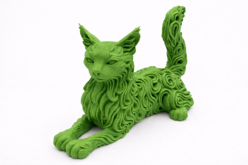Op de afbeelding: Een groene kattenbeeldhouwwerk in een liggende houding. De vacht van de kat is gedetailleerd met een wervelend patroon. Het beeldhouwwerk heeft een effen groene kleur en staat op een witte ondergrond. De kat heeft puntige oren en een lange staart.