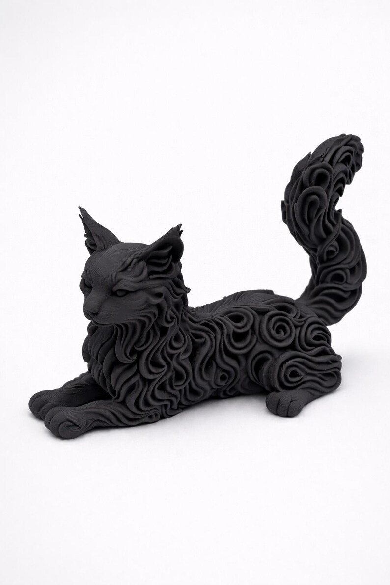 Op de afbeelding: Een zwarte kattenbeeldhouwwerk in een liggende pose. De vacht van de kat is gedetailleerd met wervelende patronen en de staart is omhoog gekruld. De sculptuur heeft puntige oren en staat tegen een witte achtergrond.