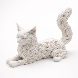 Op de afbeelding: Een witte kattenfiguur in een liggende houding. De vacht van de kat is gedetailleerd met een wervelend, gestructureerd patroon. De sculptuur heeft puntige oren en een gekrulde staart, wat een decoratief en artistiek stuk cre&euml;ert.