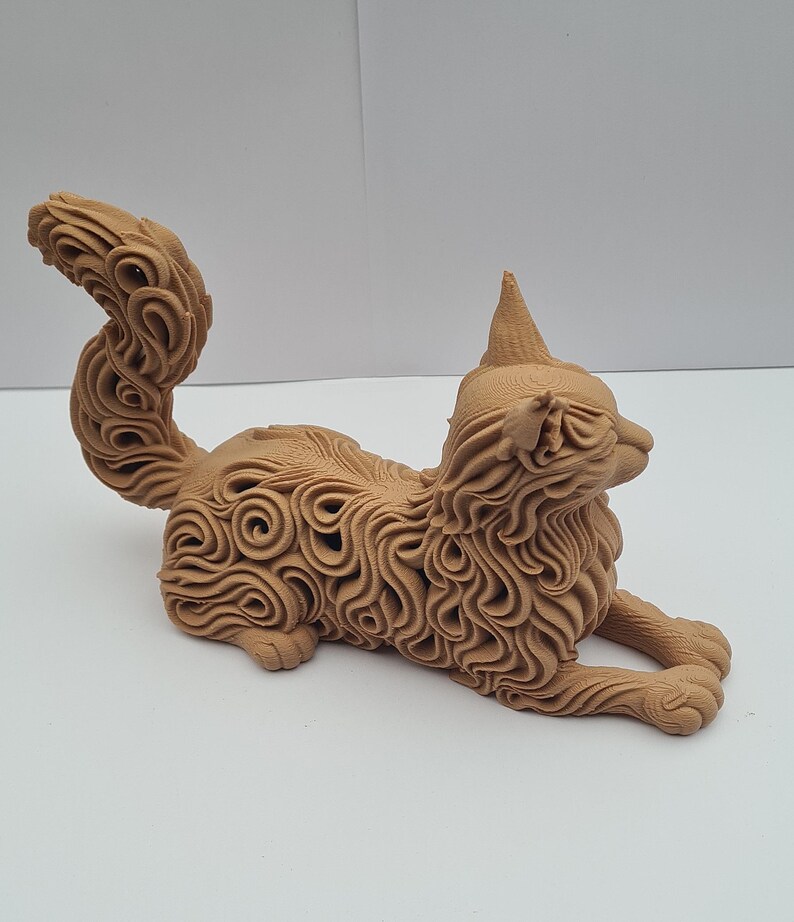 Op de afbeelding: Een gedetailleerd, bruin kattenbeeldje in een ontspannen houding. De vacht van de kat is ingewikkeld ontworpen met wervelende patronen, en het heeft een puntig oor en een gekrulde staart. Het beeldje staat op een witte ondergrond.