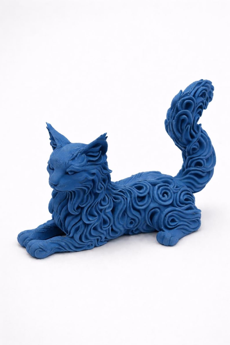 Op de afbeelding: Een gedetailleerde blauwe kattenbeeldhouwkunst in een ontspannen pose. De vacht van de kat is ingewikkeld ontworpen met wervelende patronen. De sculptuur heeft een effen blauwe kleur en rust op een witte ondergrond.