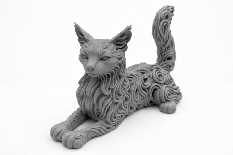 Op de afbeelding: Een grijze kattenbeeldhouwwerk in een liggende houding. De vacht van de kat is gedetailleerd met een wervelend patroon. De sculptuur heeft puntige oren en een lange, gekrulde staart. De kat ligt op een witte ondergrond.