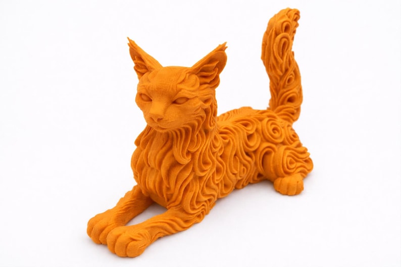 Op de afbeelding: Oranje kattenbeeld met gedetailleerde vacht en gekrulde staart. De kat ligt in een liggende houding, met uitgestrekte poten. Het beeld is gemaakt van een textuurrijk materiaal en heeft een gestileerd ontwerp. Het kattenbeeldje is een decoratief item.