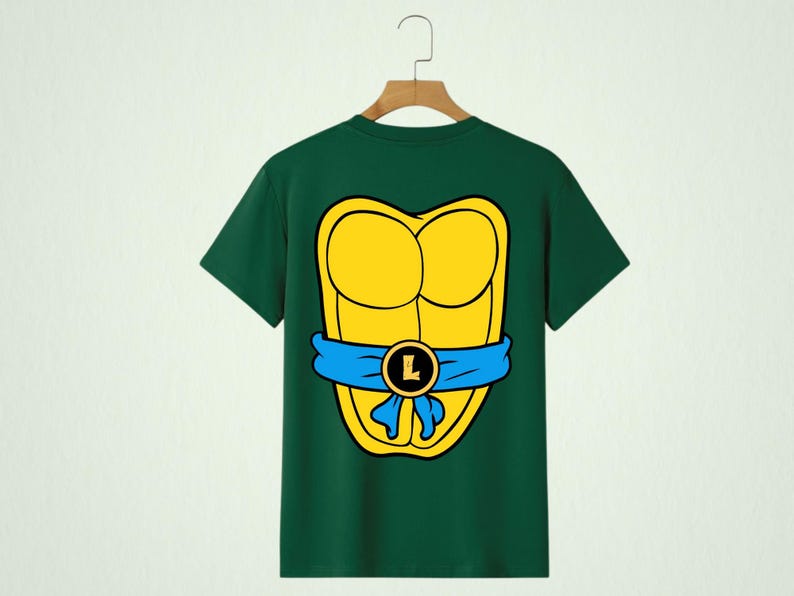 May include: Green t-shirt featuring a yellow turtle shell design with a blue belt and a gold buckle with the letter "L". The shirt is hanging on a wooden hanger.
