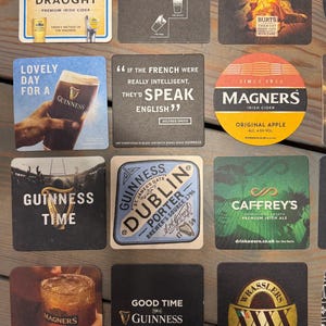 Op de afbeelding: Een verzameling vierkante en ronde drankonderzetters met logo's en teksten van Ierse merken. De onderzetters tonen logo's, teksten en afbeeldingen, waaronder het Guinness-logo en het Magners-logo.