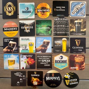 Op de afbeelding: Een verzameling bier- en cideronderzetters met verschillende logo's en tekst. Merken zijn onder andere Guinness, Magners, Rockshore en Harp. Sommige onderzetters tonen zinnen als "Lovely Day for a Guinness" en "Good Time Guinness."