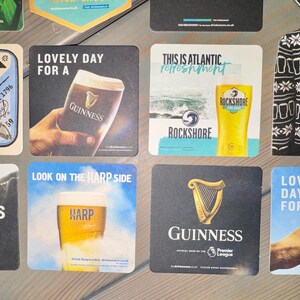Pode incluir: Cole&ccedil;&atilde;o de bases para copos quadradas com marcas de cerveja como Guinness e Harp. Os designs incluem um padr&atilde;o de camisola a preto e branco, um copo de cerveja e o texto "Lovely Day For A".