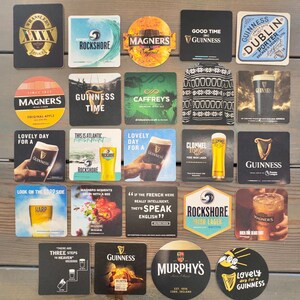 Op de afbeelding: Een verzameling vierkante en ronde drankonderzetters met logo's van verschillende bier- en cider merken. Onderzetters met logo's en tekst voor Guinness, Magners, Rockshore, Harp en Murphy's. Sommige onderzetters hebben afbeeldingen van drankjes.