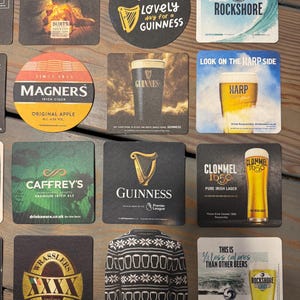 Op de afbeelding: Een verzameling bierviltjes met verschillende merken, waaronder Guinness, Magners en Rockshore. De viltjes tonen logo's en teksten zoals "Lovely day for a Guinness" en "Original Apple".