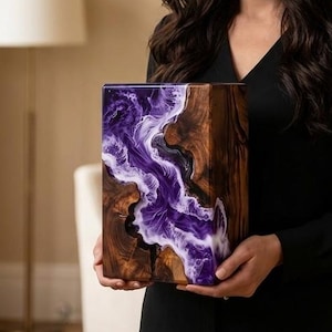 May include: A wooden block with a purple and white resin design. The wood has a natural grain pattern, and the resin flows like a river. The block is rectangular and appears to be a decorative item or a piece of art.