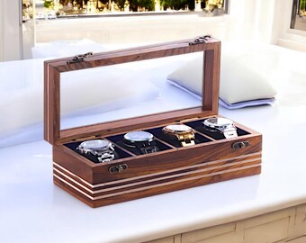 May include: A wooden watch display case with a glass top, showcasing four watches with silver and gold tones. The case is rectangular with a dark brown finish and decorative metal accents. The interior features individual compartments with blue velvet lining.