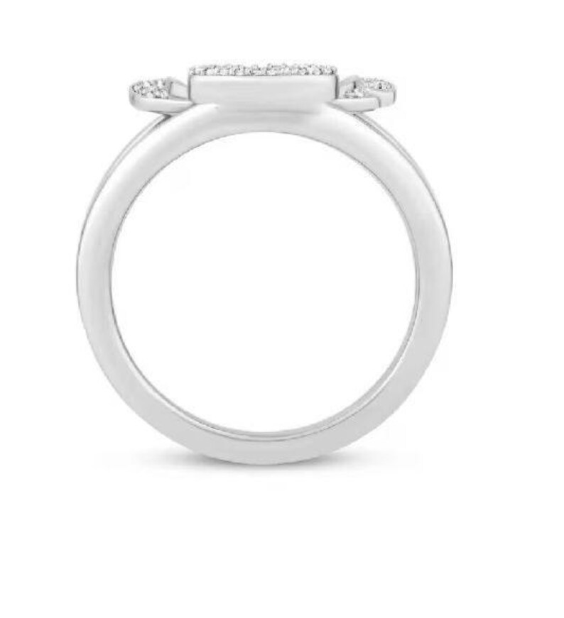 Op de afbeelding: Een zilveren ring met een rechthoekige middensteen en kleinere stenen aan de zijkanten. De ring staat tegen een witte achtergrond, waardoor het gepolijste metaal en de sprankelende details worden benadrukt. Dit sieraad is een klassiek ontwerp.