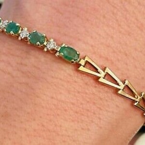 May include: Gold bracelet featuring oval emeralds and small diamonds. The bracelet has a geometric design with triangular links. The gemstones are set in a gold band, creating a luxurious and elegant piece of jewelry.