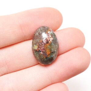 May include: Oval cabochon gemstone with copper inclusions. The stone is a mix of green, brown, and copper colors.