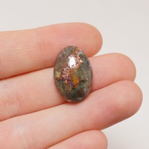 May include: Oval cabochon gemstone with a green, brown, and copper color pattern. The stone has a smooth, polished surface.